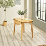 Natural wood round dropleaf table with one leaf folded down in bright room with wooden floor and window