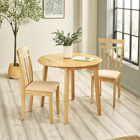 Two light wood dining chairs with beige padded seats and round table in a room with light wood floor and plant