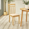 Light wood dining chair with beige cushion next to matching round light wood table in natural-tone room