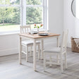 Square ivory oak dining table with two matching chairs in bright dining room