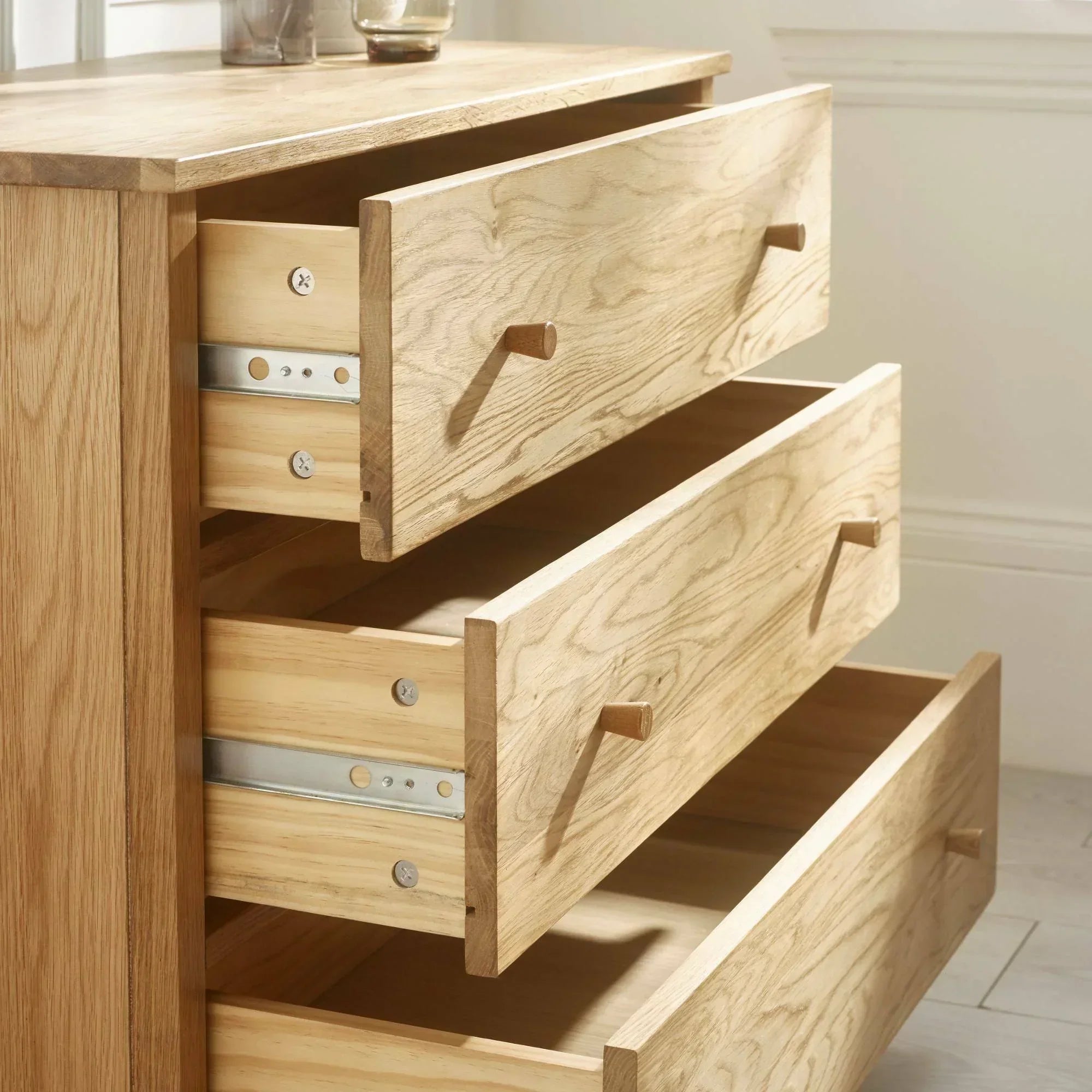 Oak chest of drawers with three open drawers showing wood grain and metal runners
