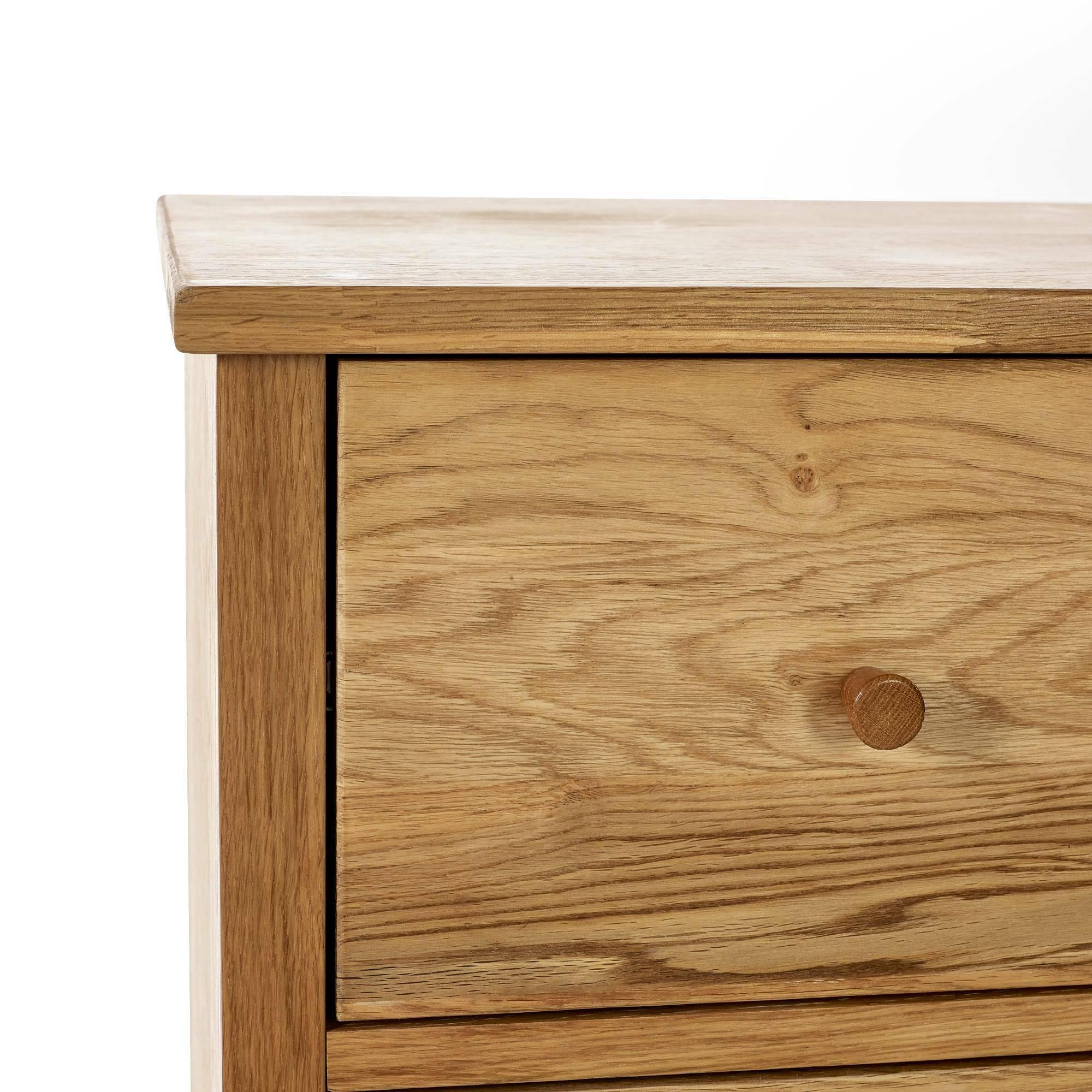 Closeup of oak chest of drawers corner showing wood grain and round wooden drawer knob