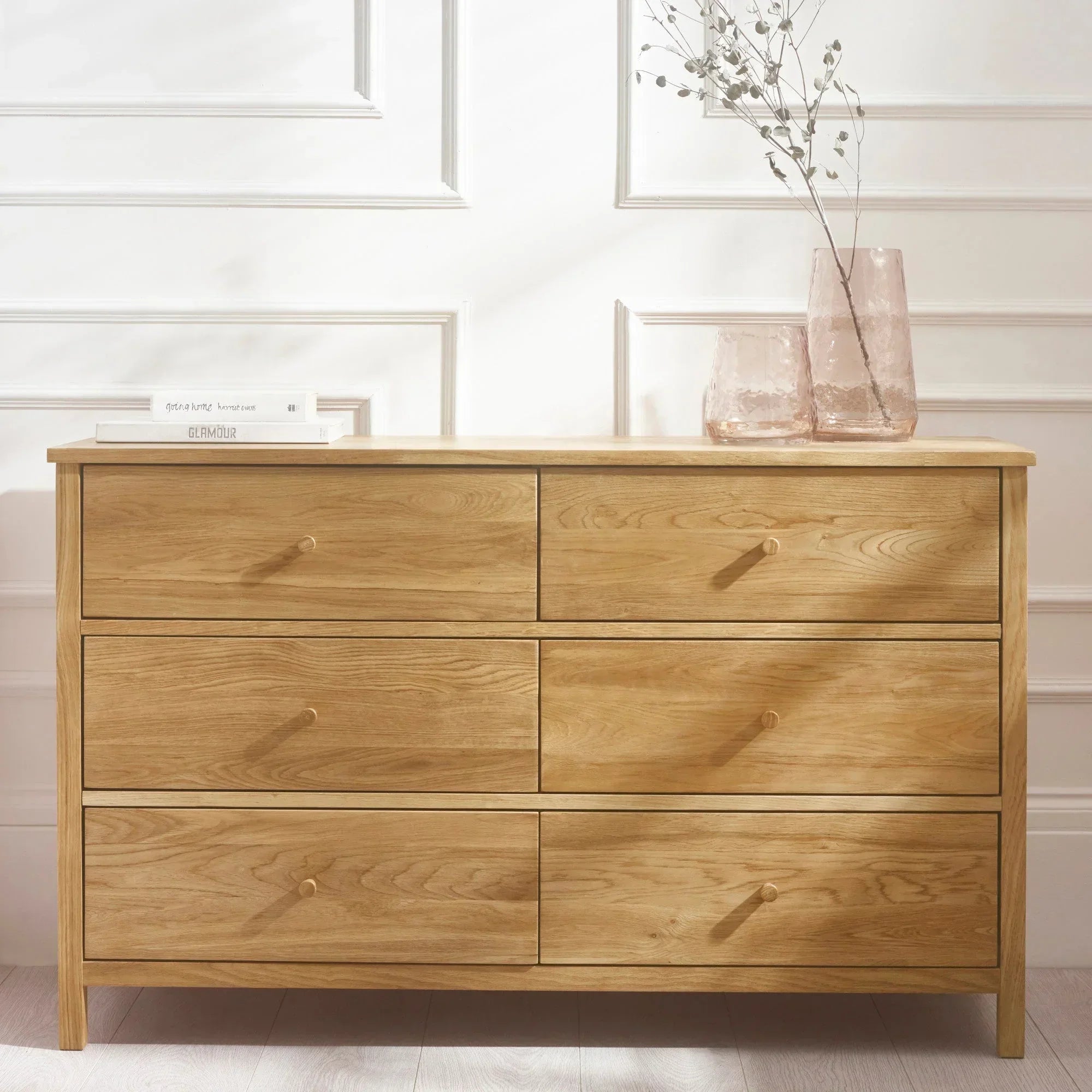 Six drawer oak chest with books and glass vases in a bright modern room