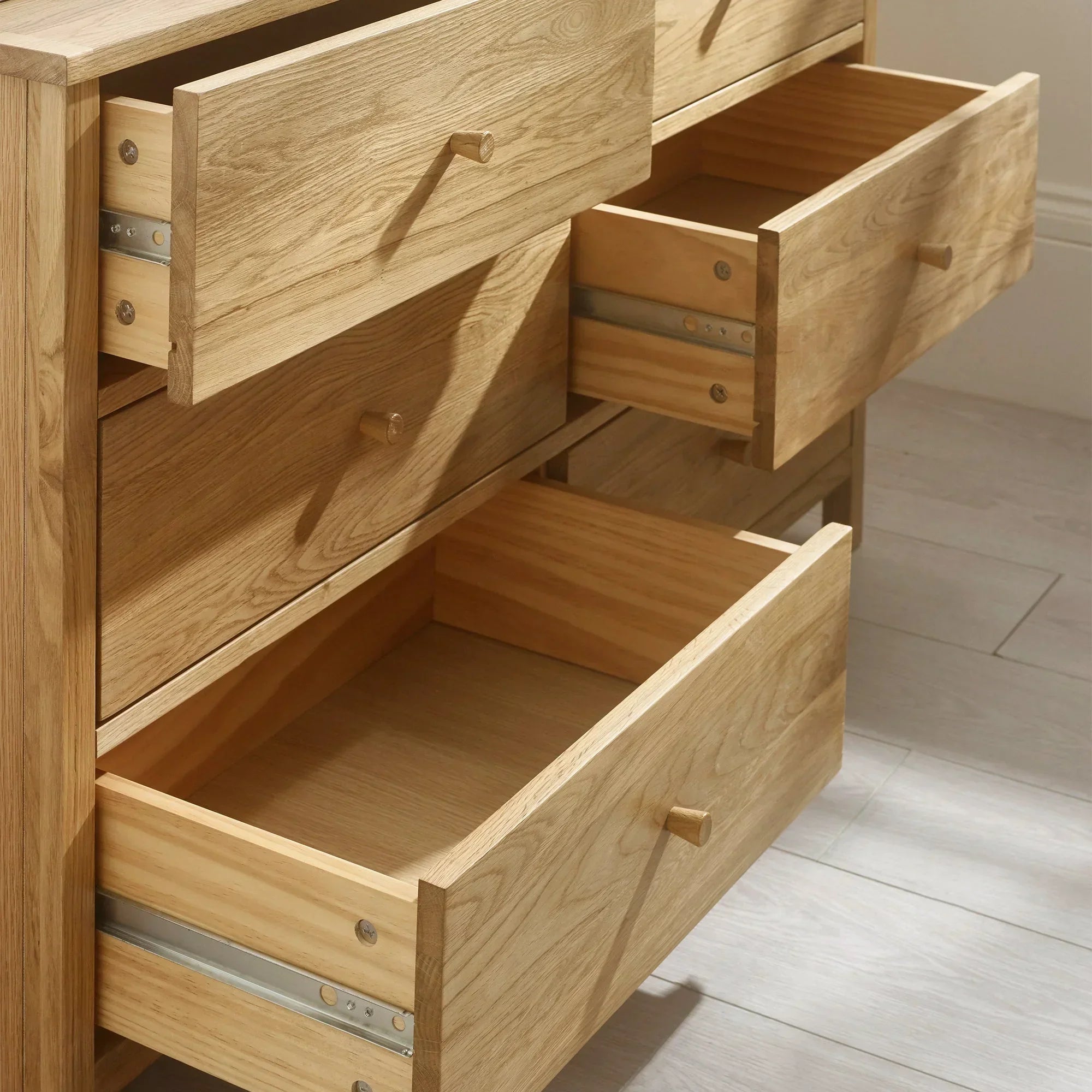 Oak chest of drawers with open drawers on light wood floor