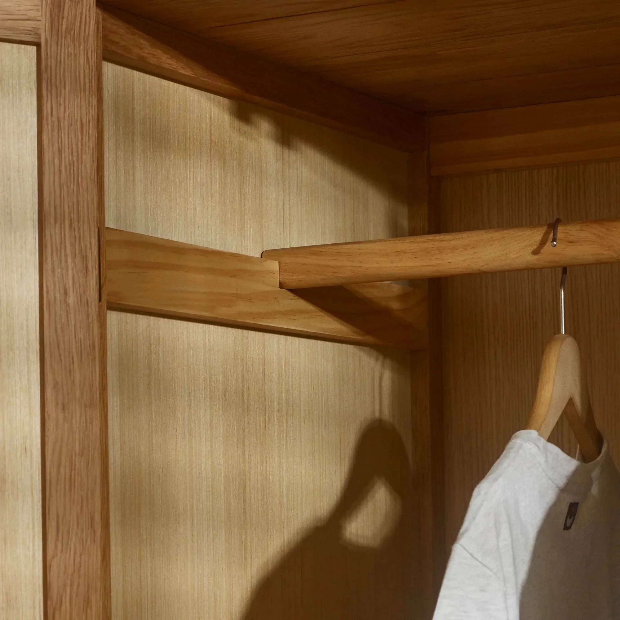 Oak wardrobe interior with wooden hanging rail and shirt on hanger
