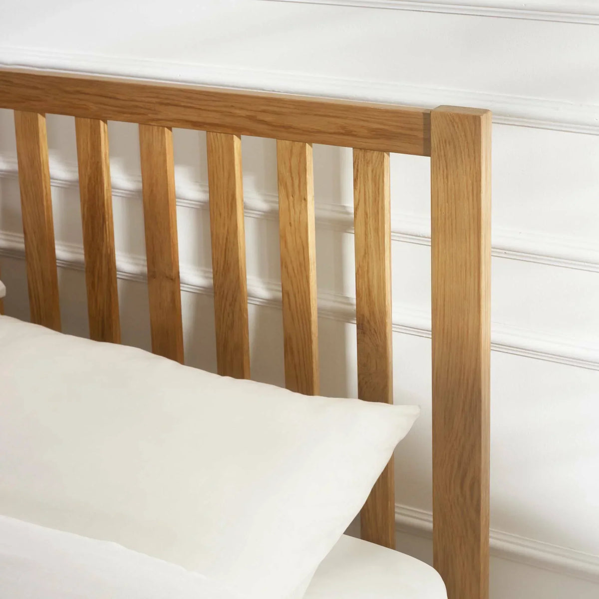 Oak double bed headboard with vertical slats and white bedding detail
