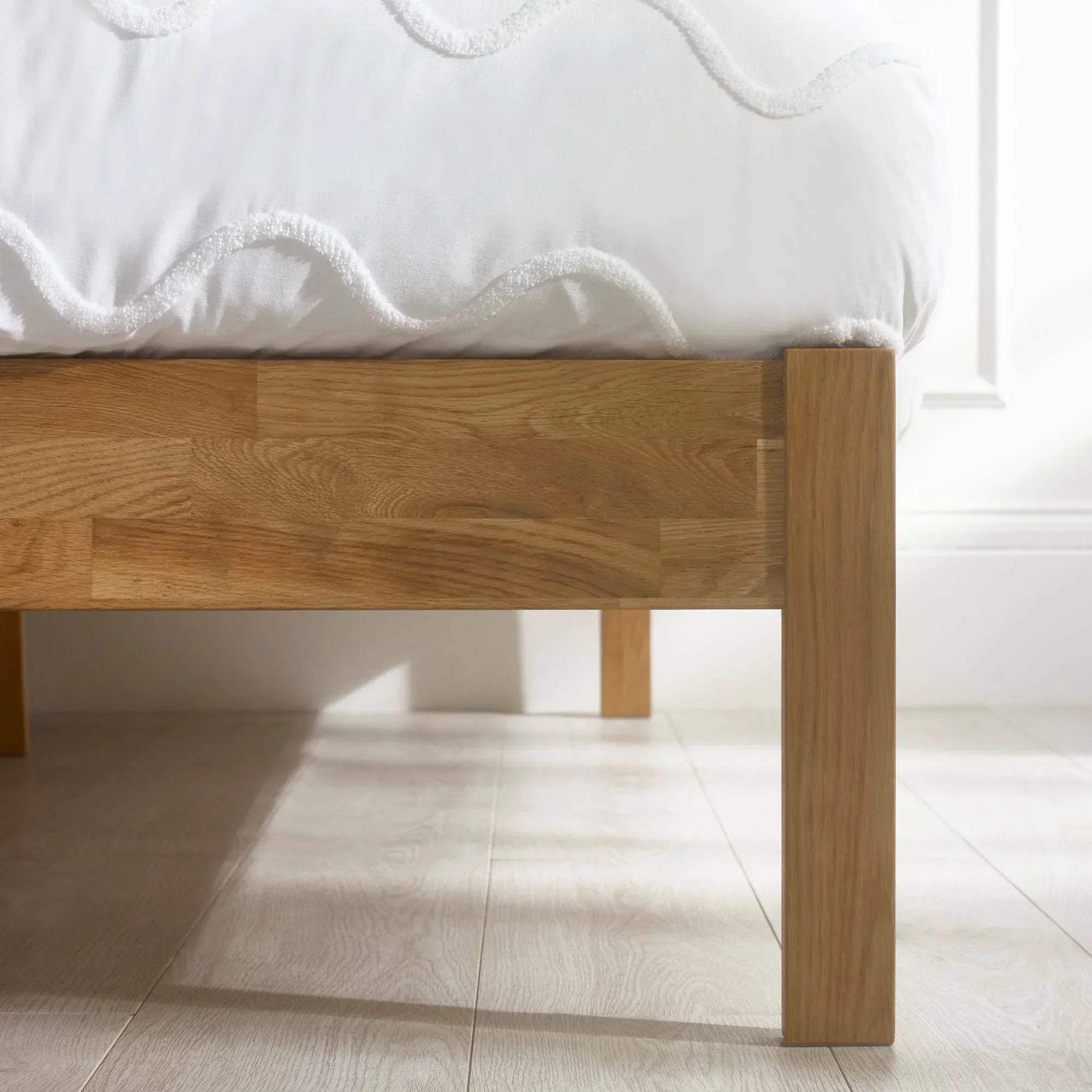 Close view of oak double bed frame leg and side panel on light wood flooring