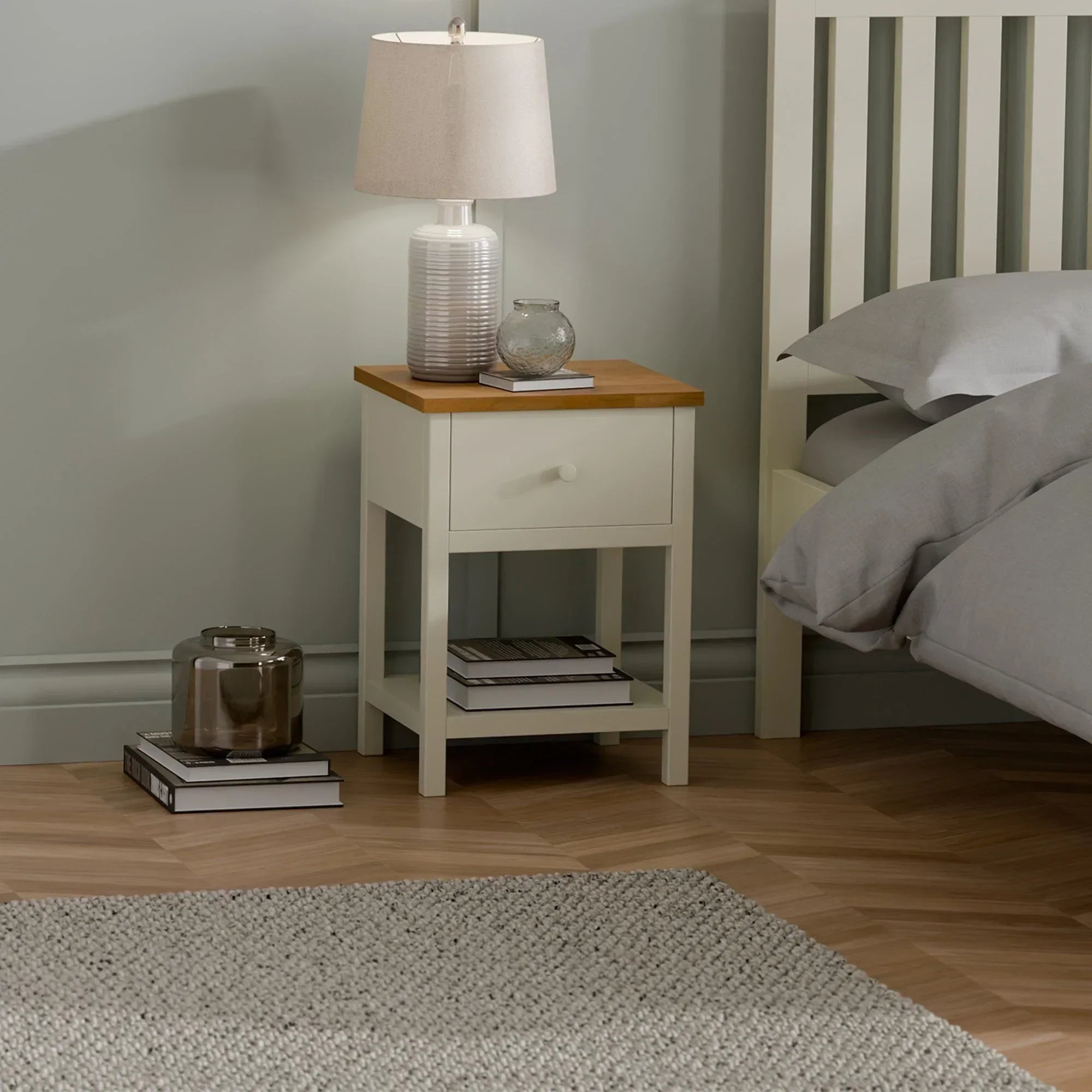 Ivory oak bedside table with single drawer, lamp, and books in modern bedroom setting