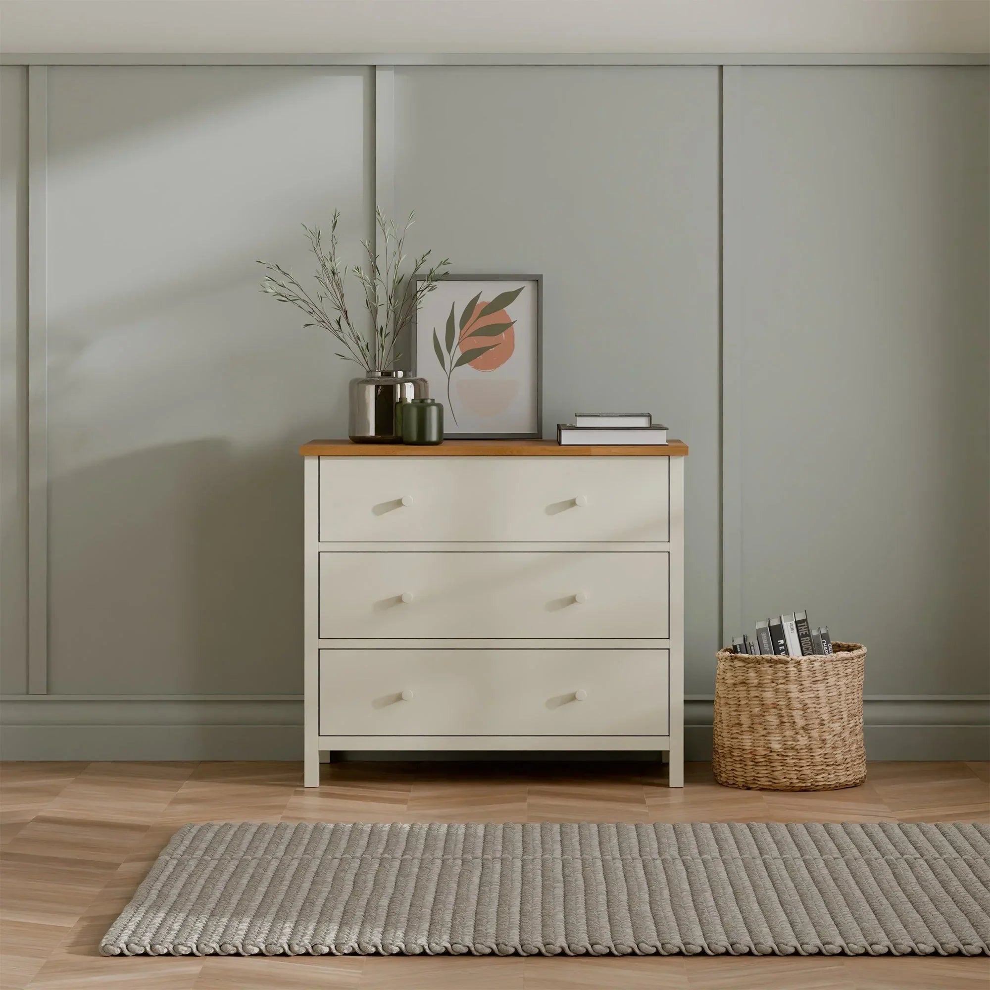 Ivory three drawer chest with oak top in modern bedroom, decorated with vase and artwork