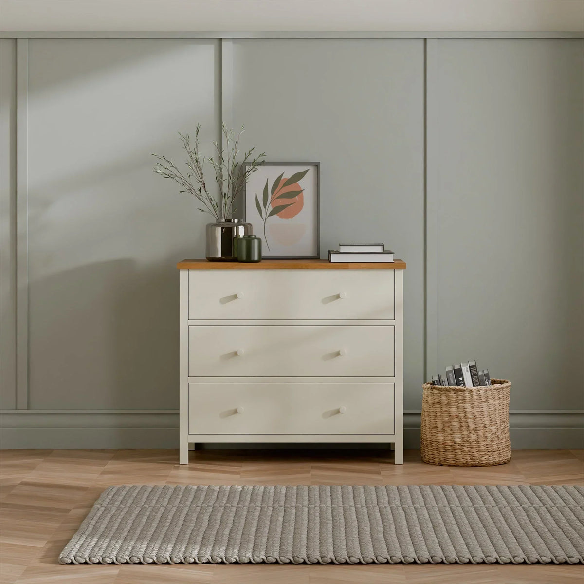 Ivory three drawer chest with oak top in modern bedroom, decorated with vase and artwork