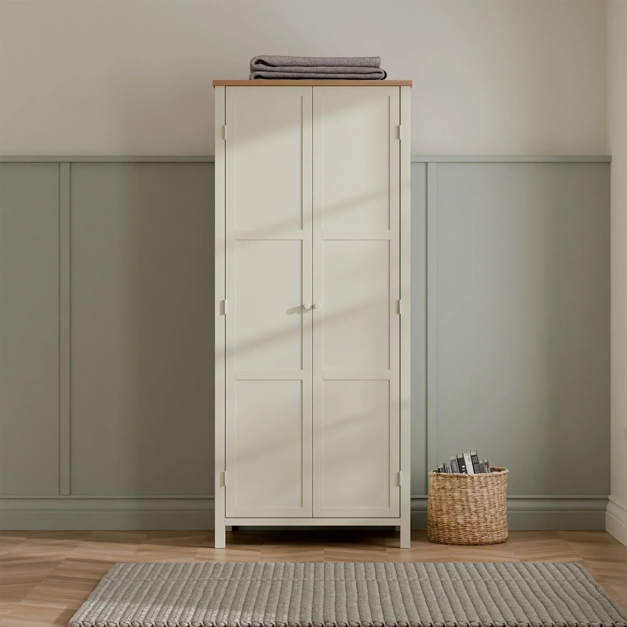 Ivory and oak wardrobe with double doors in a modern bedroom, top folded blanket, basket nearby