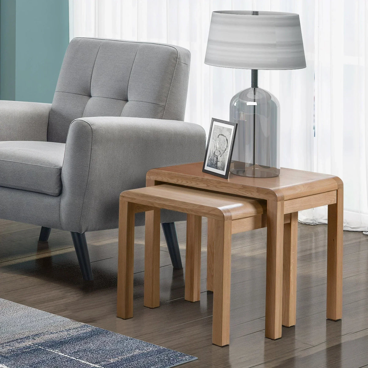 Oak nest of tables set beside grey armchair with lamp and photo frame on top