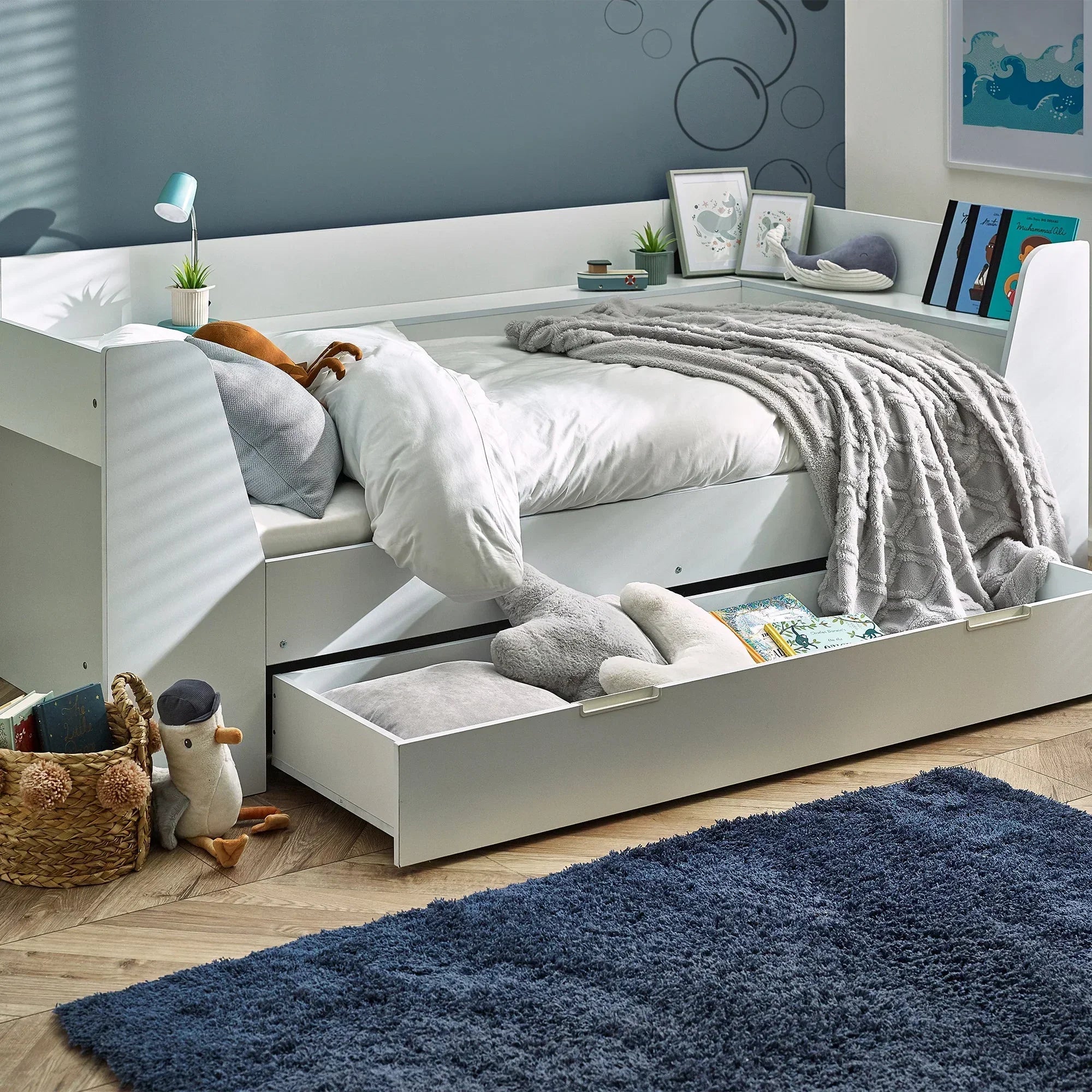 White daybed with trundle drawer, grey blanket, soft toys and books in modern kids room