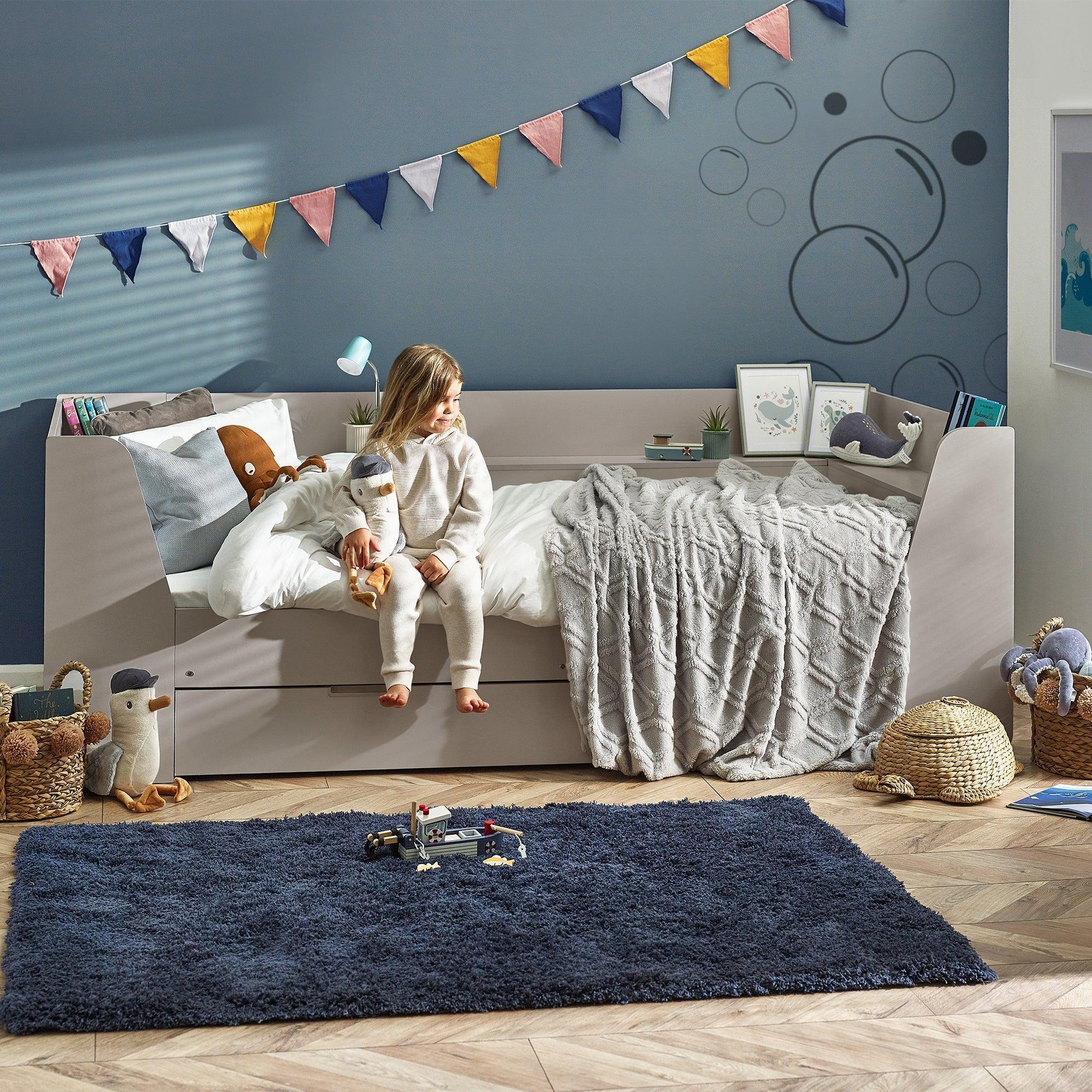 Taupe cyclone daybed with grey throw and child in modern kids bedroom with toys and rug