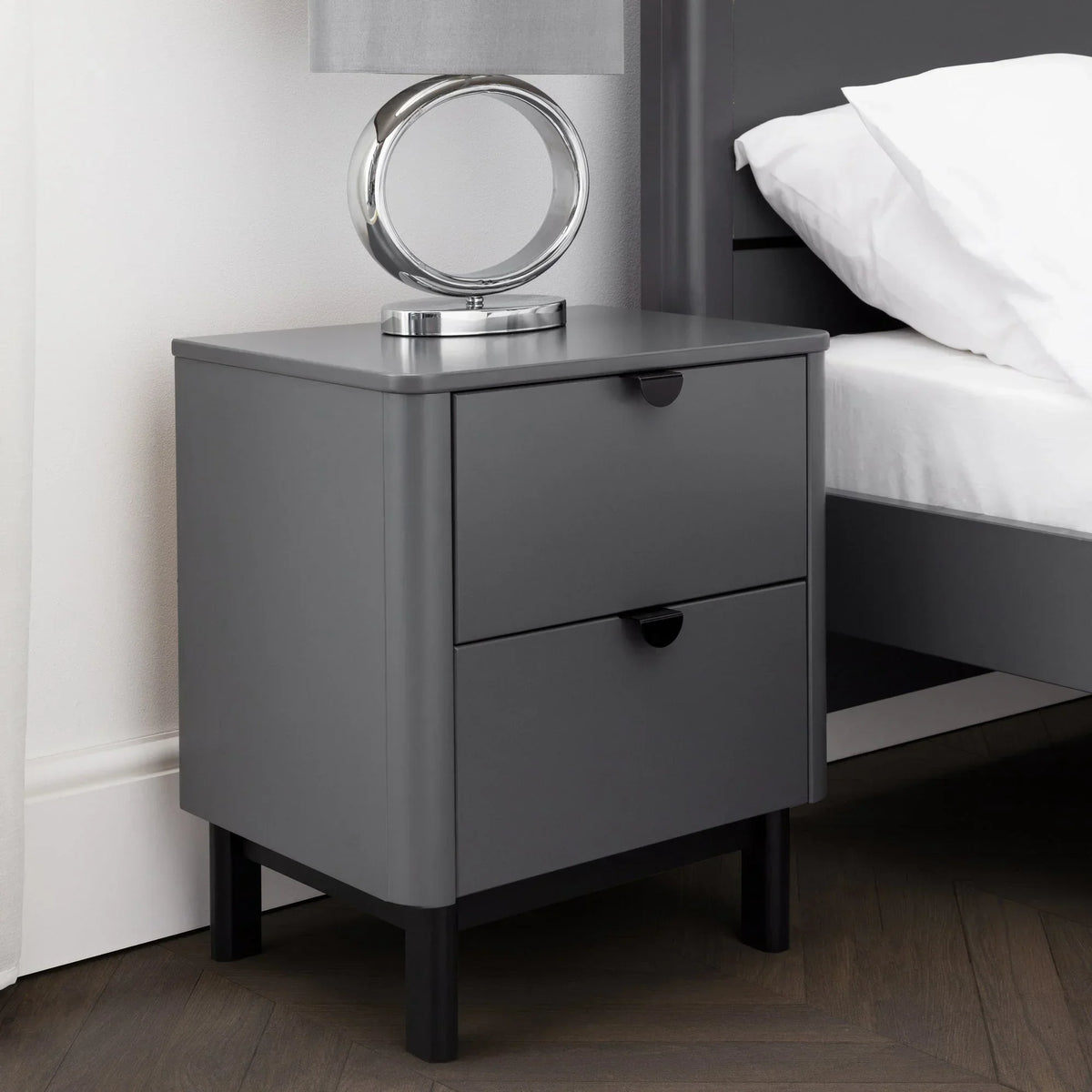 Grey two drawer bedside table with modern lamp beside bed on wood floor