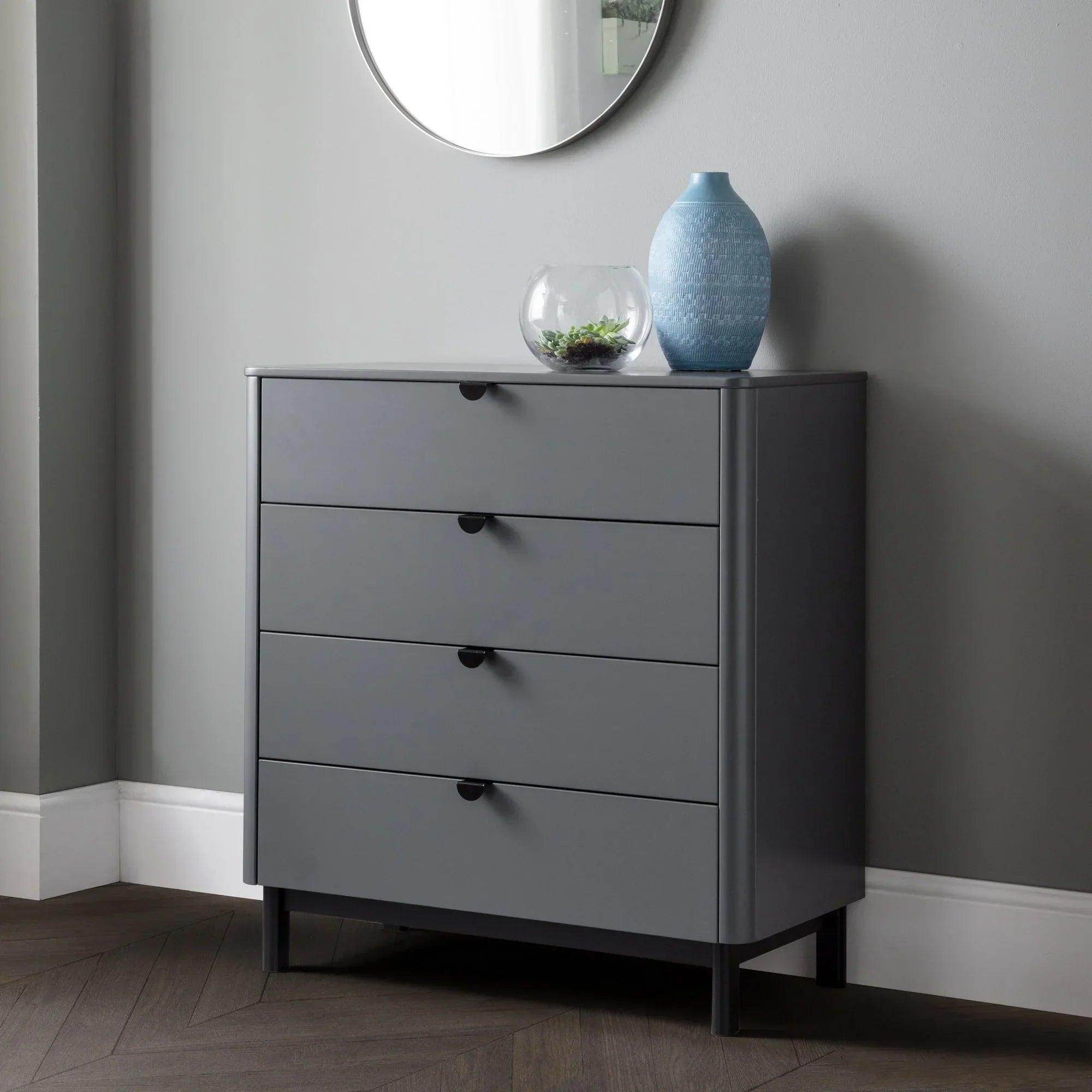 Grey 4 drawer chest with round mirror above, blue vase and glass bowl on top