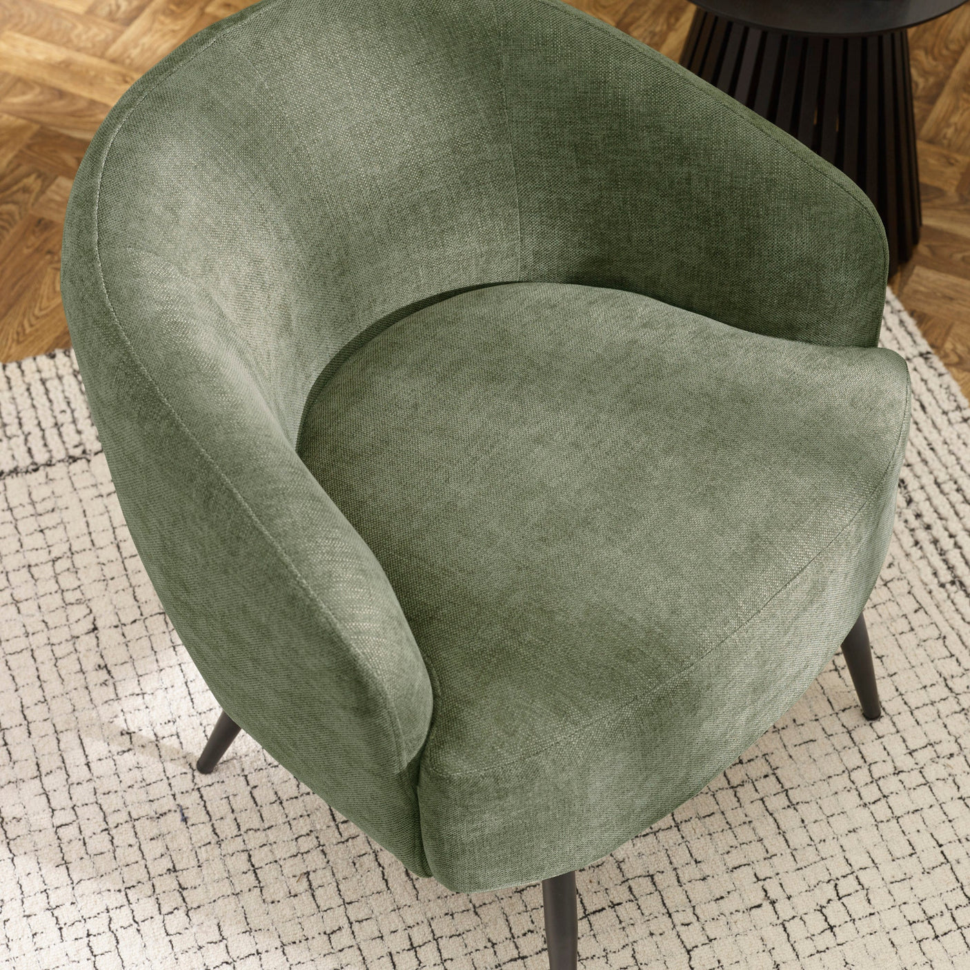 Top angled view of green fabric accent chair showing round seat and curved back on patterned rug.