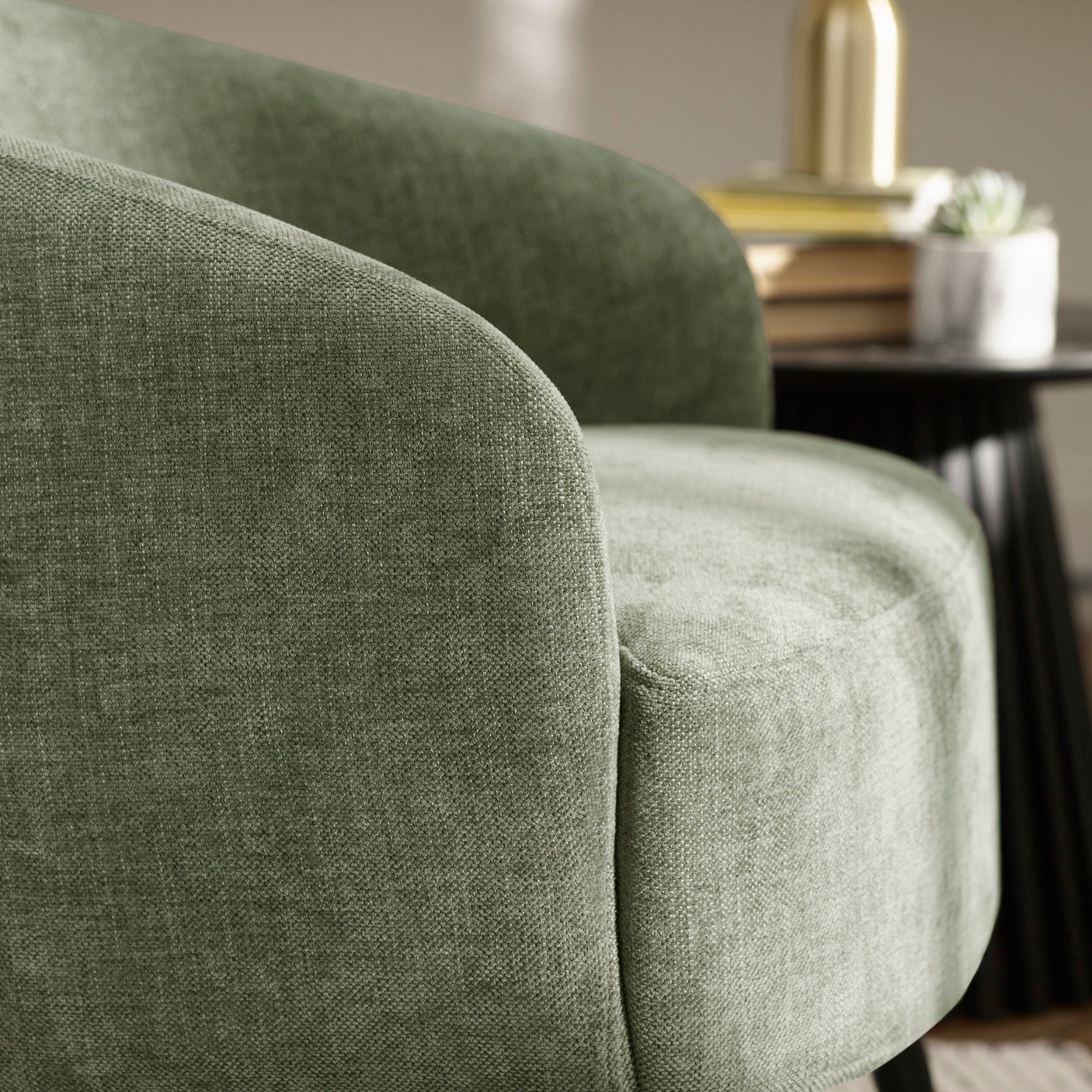Close-up detail of green fabric barrel chair curved back and armrest with neutral decor background.