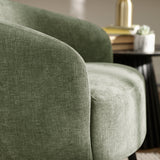 Close-up detail of green fabric barrel chair curved back and armrest with neutral decor background.