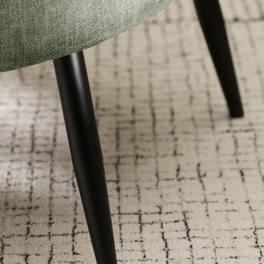 Close-up view of black tapered leg and patterned rug under green fabric accent chair.