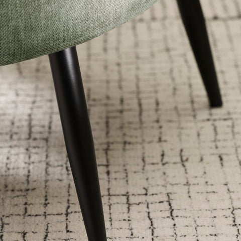 Close-up view of black tapered leg and patterned rug under green fabric accent chair.