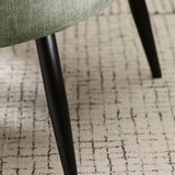Close-up view of black tapered leg and patterned rug under green fabric accent chair.