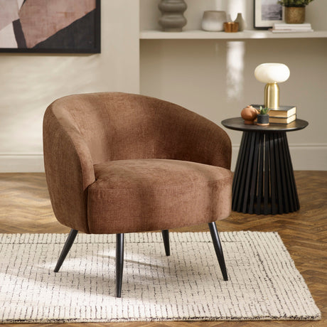 Brown fabric accent chair on a white rug in living room with side table, lamp, and decor