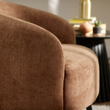 Close-up of brown fabric accent chair curved back and black tapered leg with side table in background