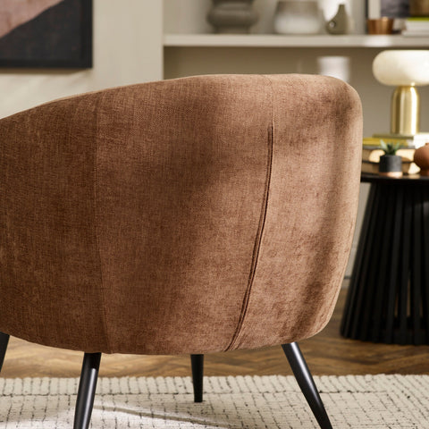 Brown fabric accent chair with curved back and slim black legs on a white textured rug in a modern room.