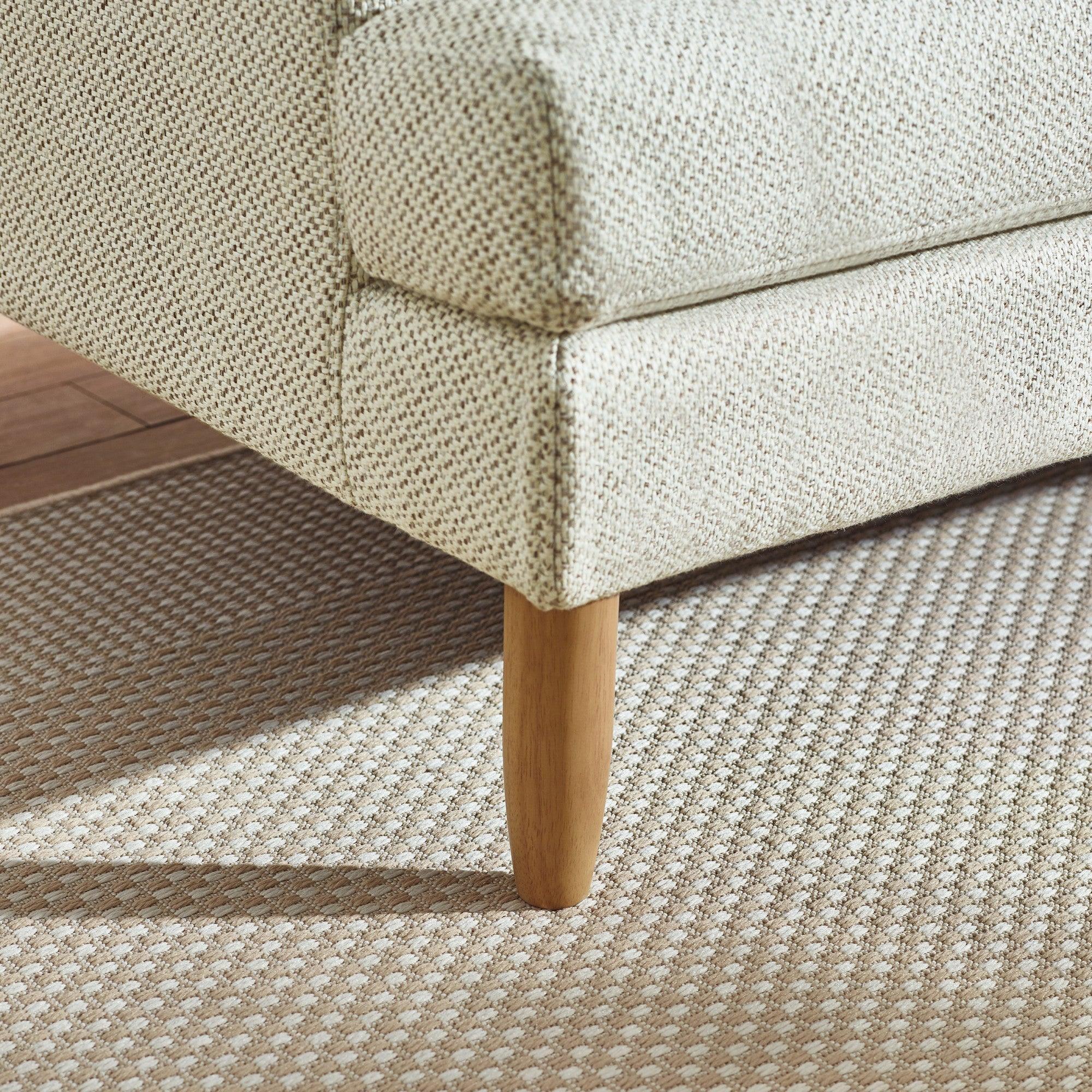 Fabric sofa corner with wooden leg on patterned beige rug, close-up view
