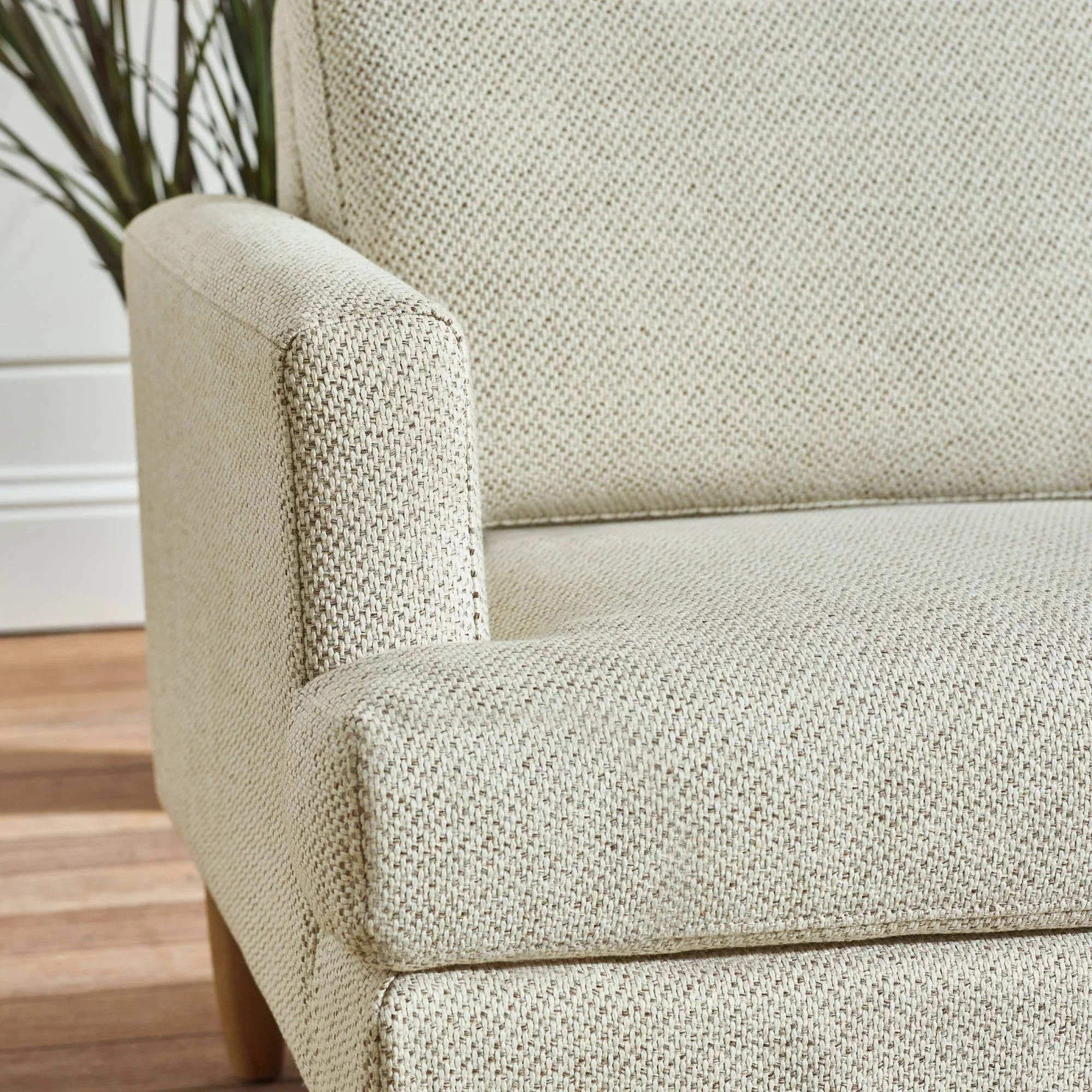 Beige fabric sofa armrest and seat closeup with textured upholstery and wooden leg