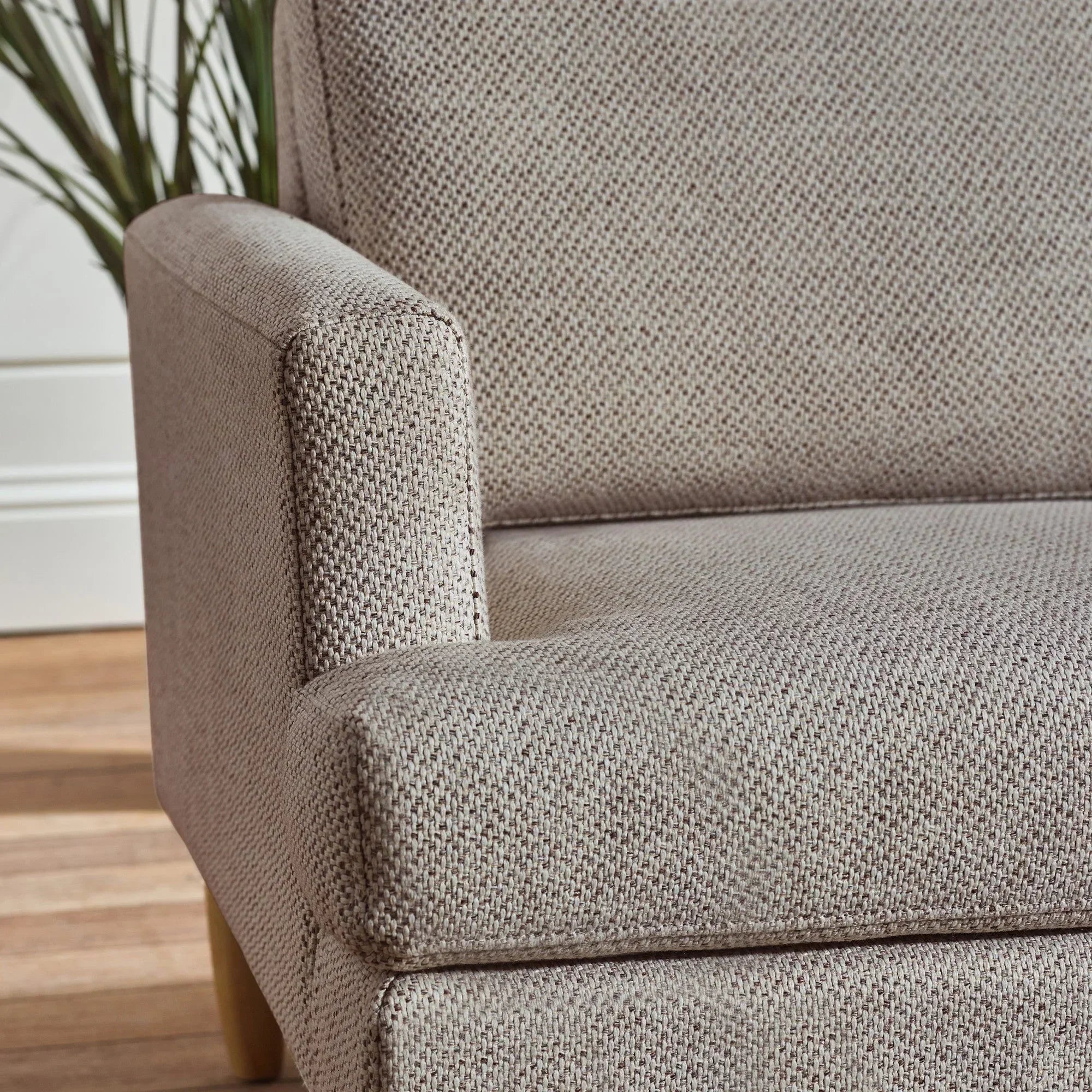 Close-up of beige fabric sofa armrest and seat with textured upholstery