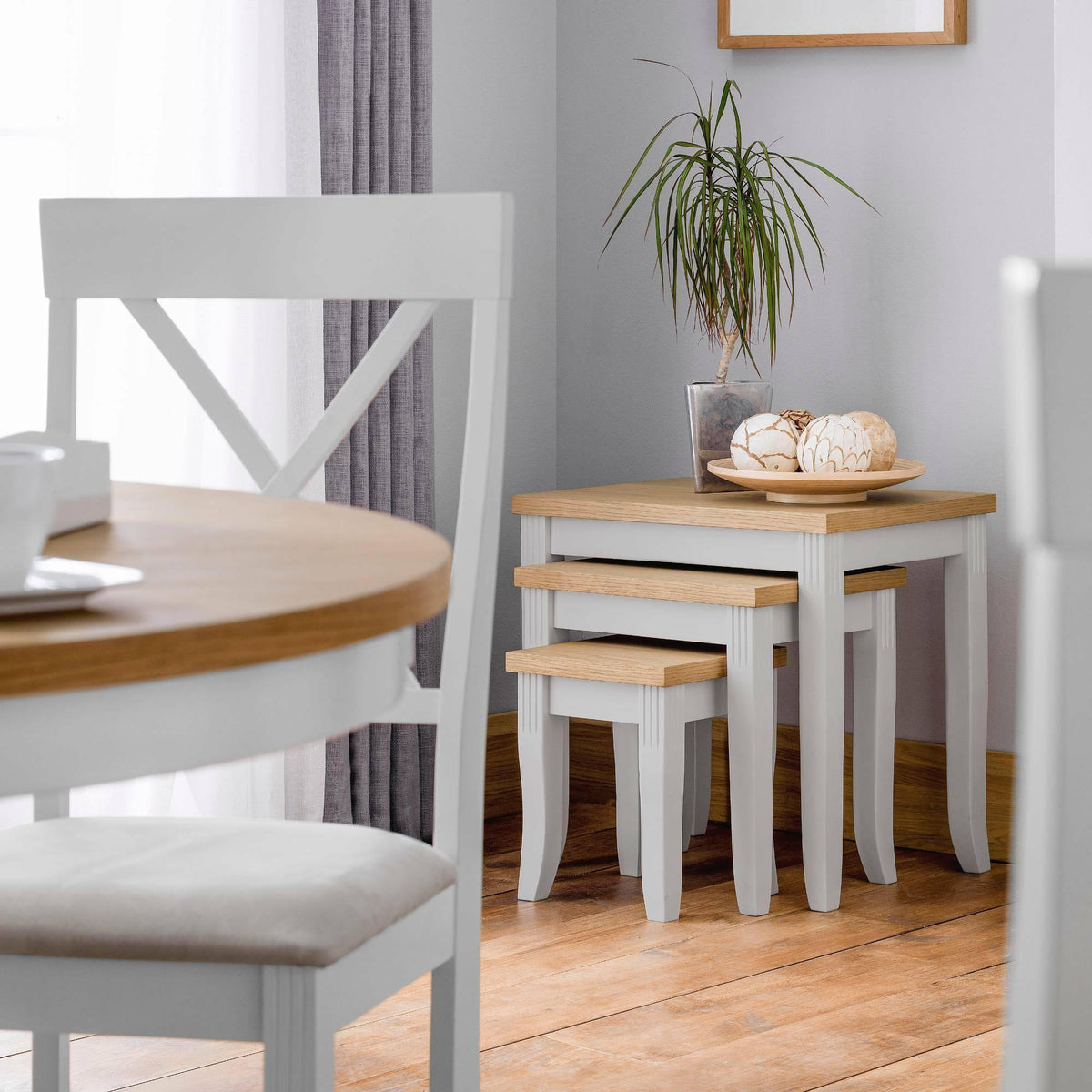 Elephant grey nest of tables with oak tops in bright dining room, plant and decor on top