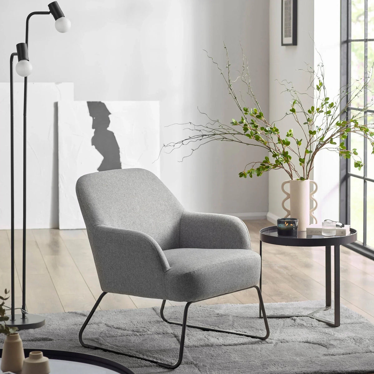 Grey accent chair with slim metal legs beside round side table and floor lamp in modern living room