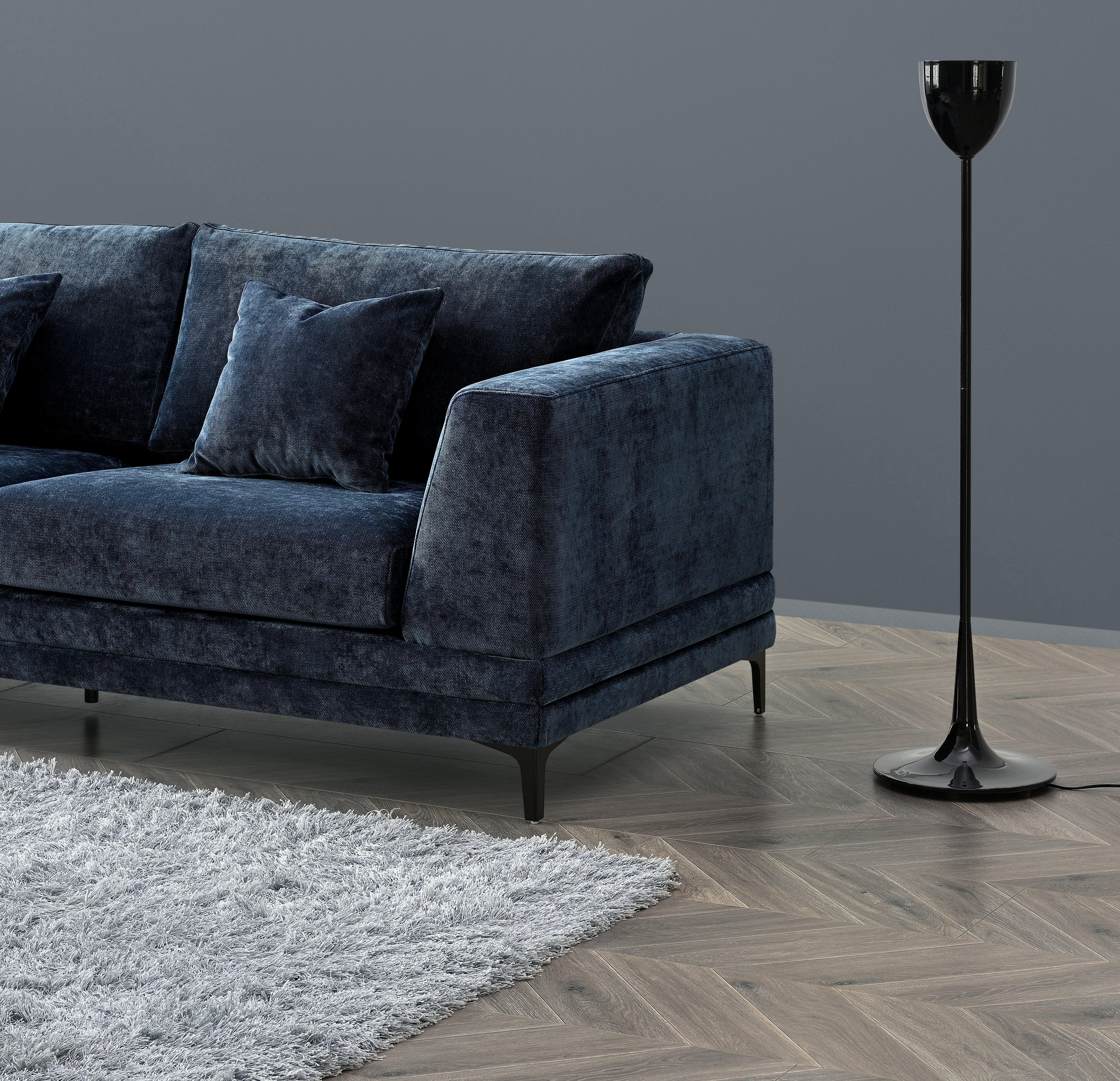 Dark blue velvet sofa with matching cushions beside modern black floor lamp on wooden herringbone floor