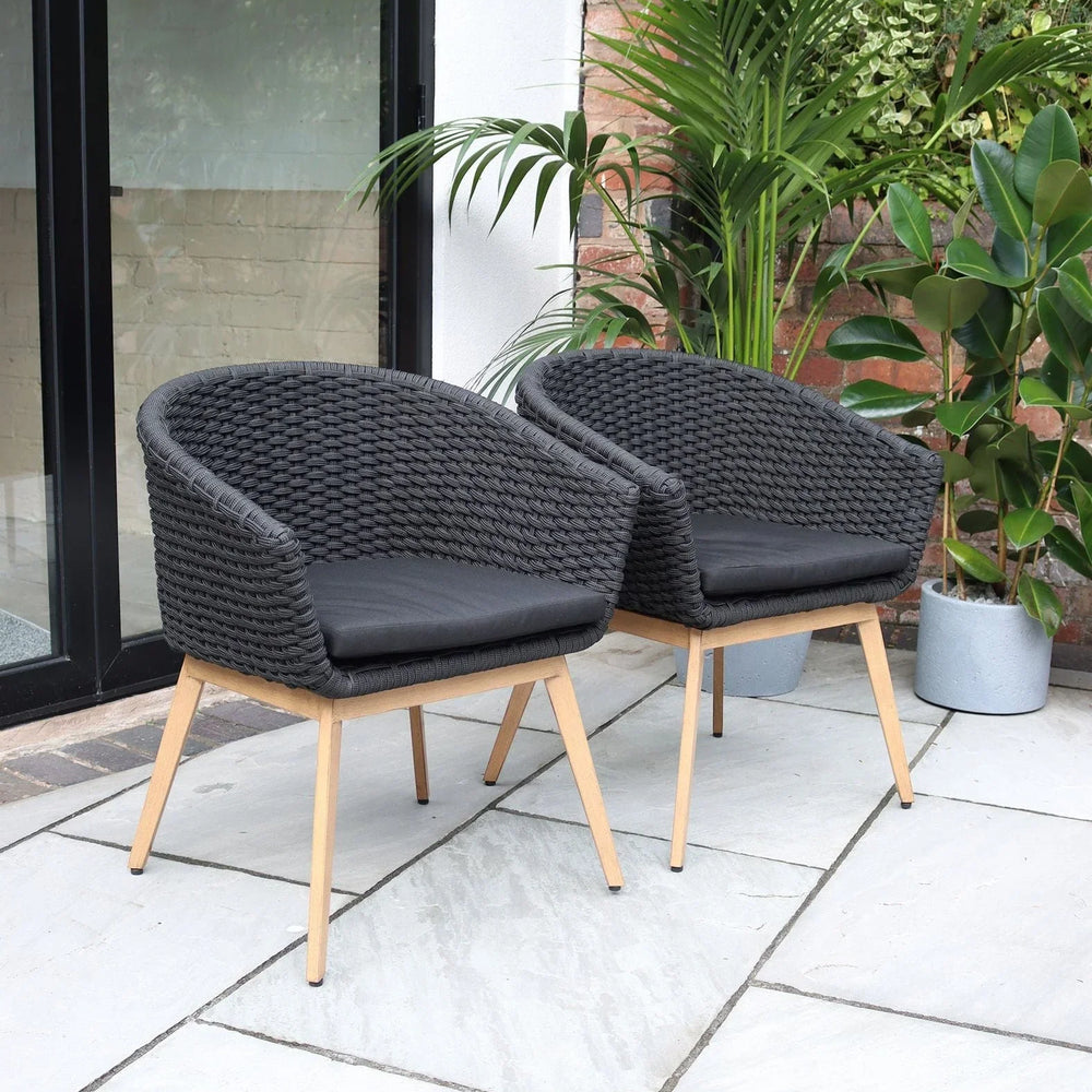 Pair of black rattan garden chairs with cushions on patio beside plants