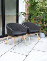 Pair of black rattan garden chairs with cushions on patio beside plants