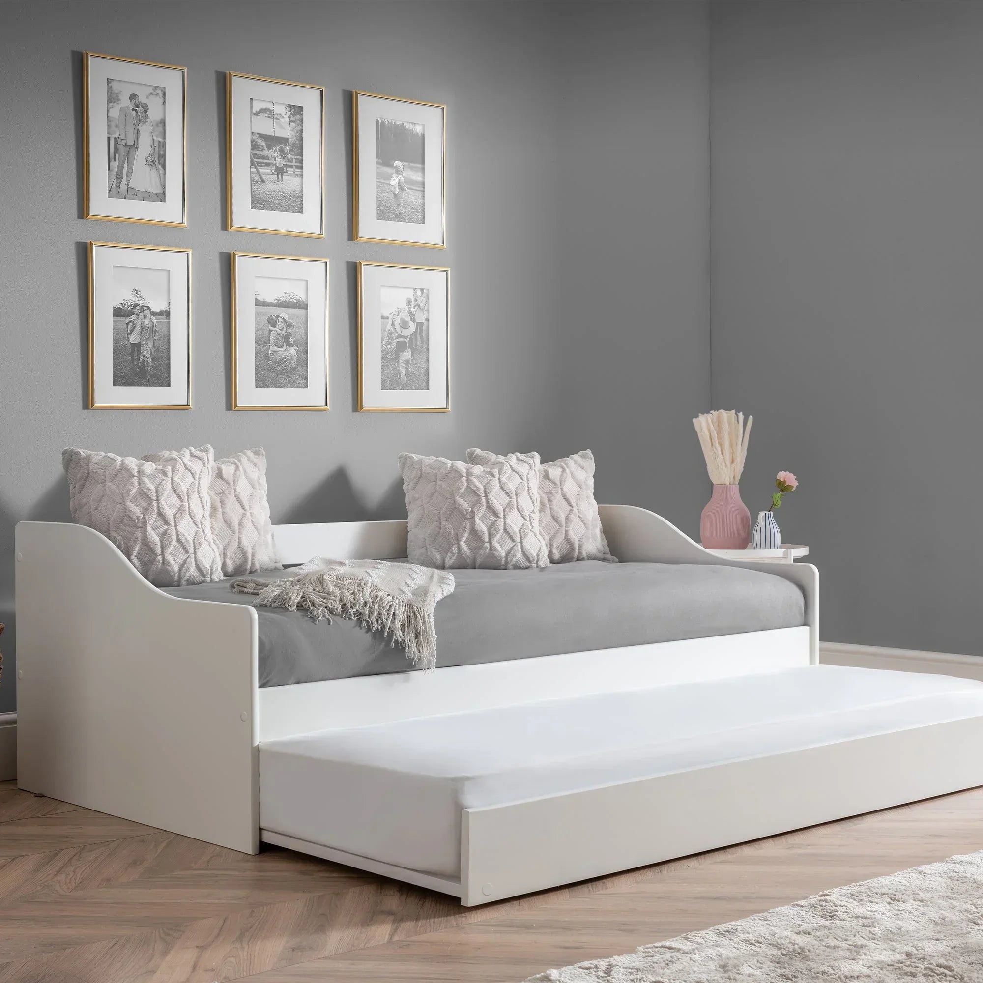 White single daybed with pull-out trundle in modern grey room, two textured cushions, wall art