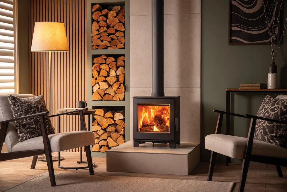 A modern wood burning stove in a stylish living room with comfortable seating and a stack of firewood.