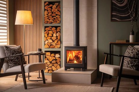 A modern wood burning stove in a stylish living room with comfortable seating and a stack of firewood.