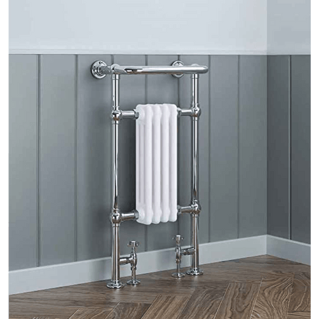 Chrome towel radiator with a white towel against a gray paneled wall.