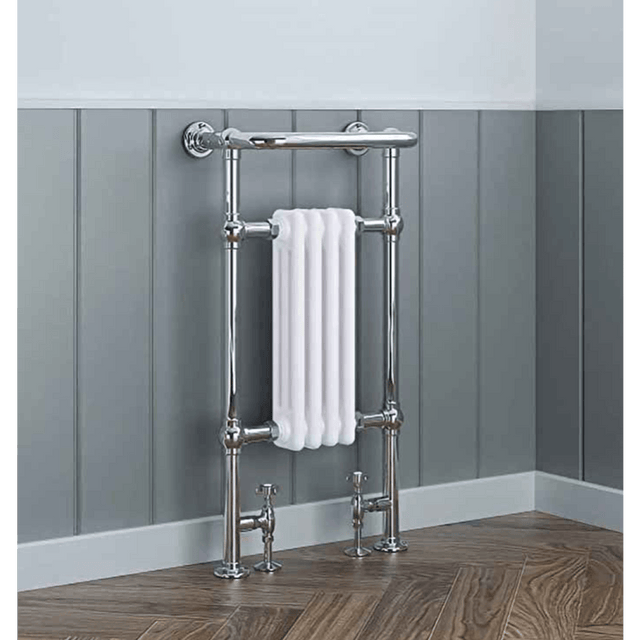 Chrome towel radiator with a white towel against a gray paneled wall.