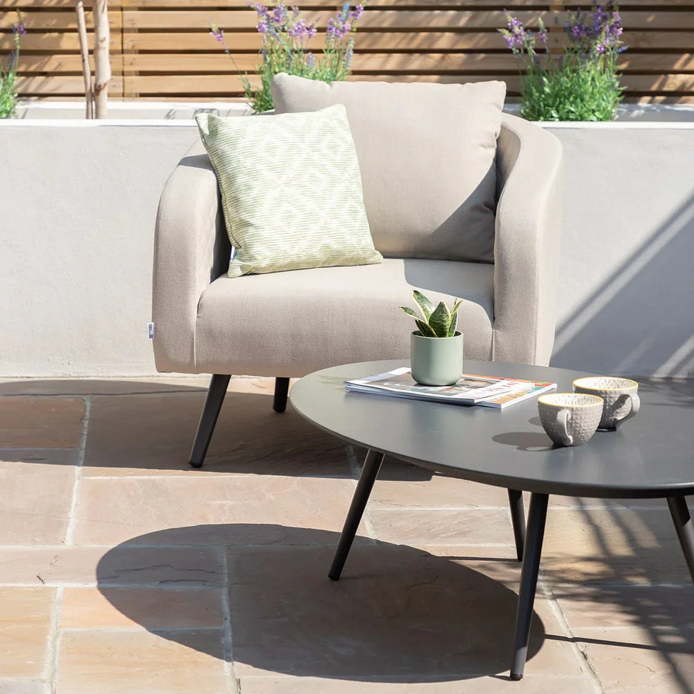 Beige outdoor armchair with green patterned cushion beside round black garden coffee table