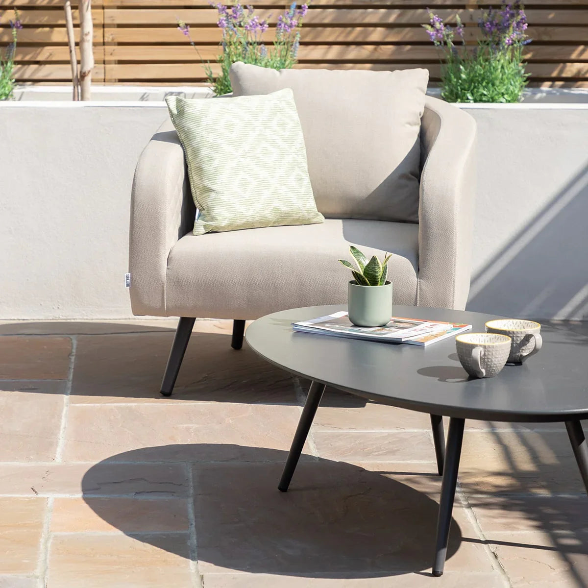 Beige outdoor armchair with green patterned cushion beside round black garden coffee table