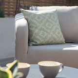 Light grey outdoor sofa with green patterned cushion and coffee cups on a table