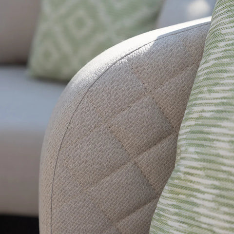 Close up of beige fabric sofa arm with quilted stitching and green patterned cushion