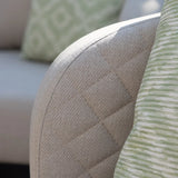 Close up of beige fabric sofa arm with quilted stitching and green patterned cushion