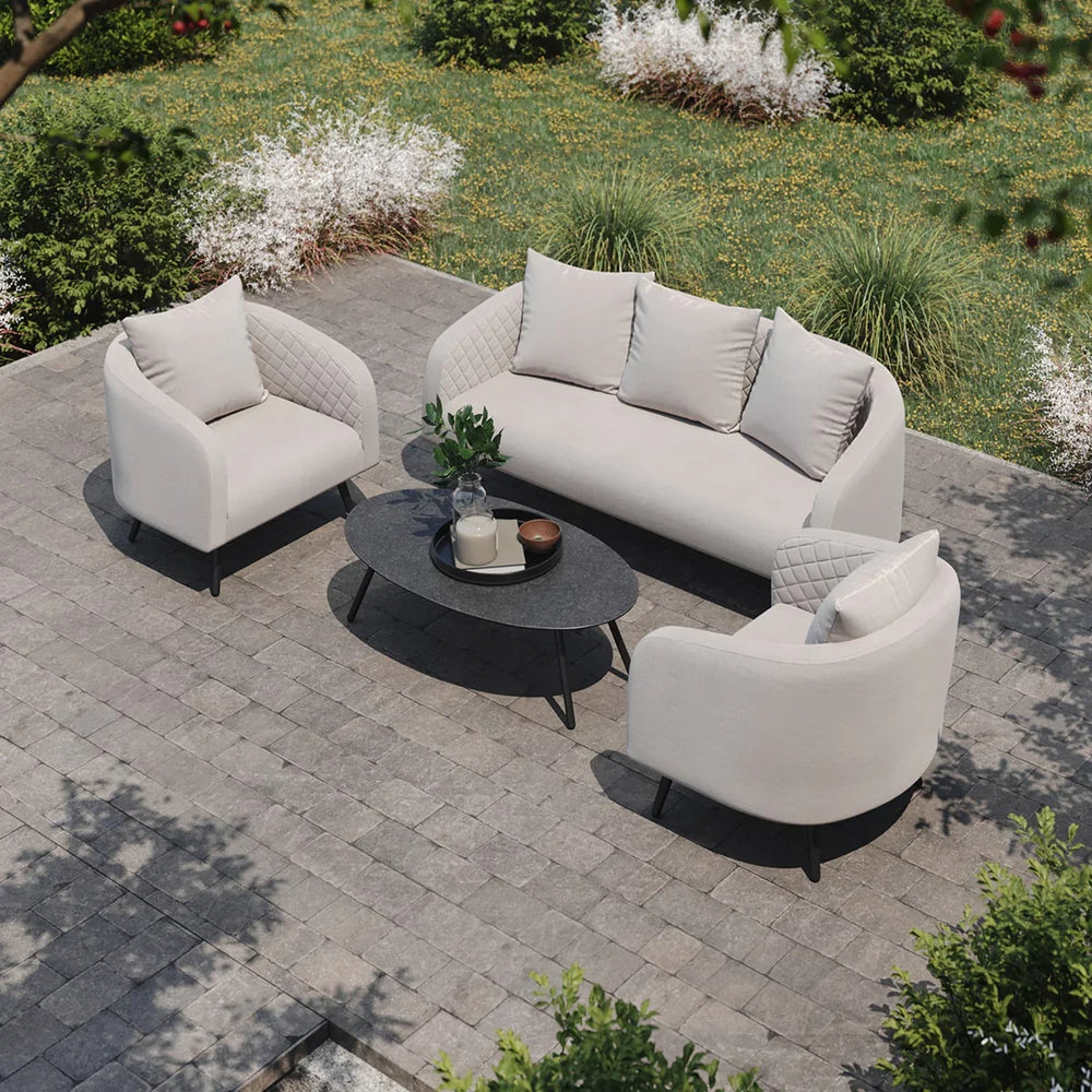 Beige outdoor sofa set with two armchairs and oval coffee table on paved patio