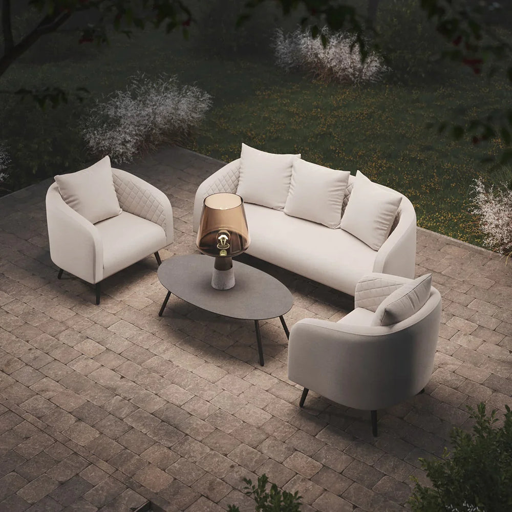 Cream outdoor sofa set with two armchairs, oval coffee table, and lamp on patio