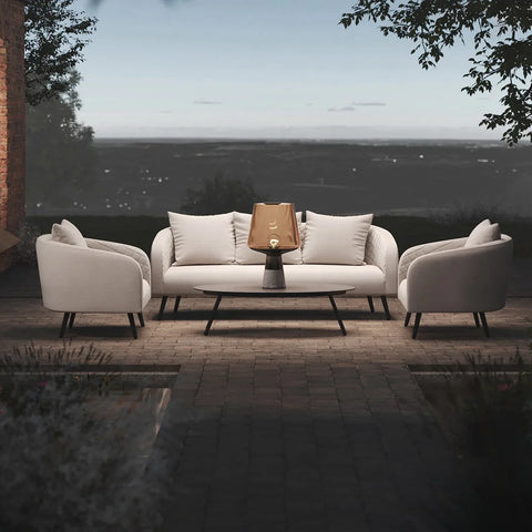 Outdoor sofa set with cream fabric armchairs, coffee table, and lantern on patio at dusk